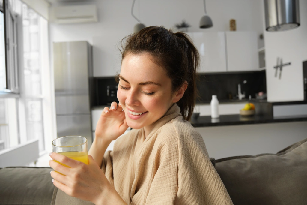 gorgeous-brunette-woman-smiles-coquettish-sits-sofa-with-freshly-made-glass-orange-juice.webp